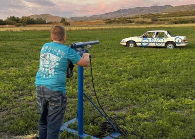 A young man taking aim at the target car with a corn cannon